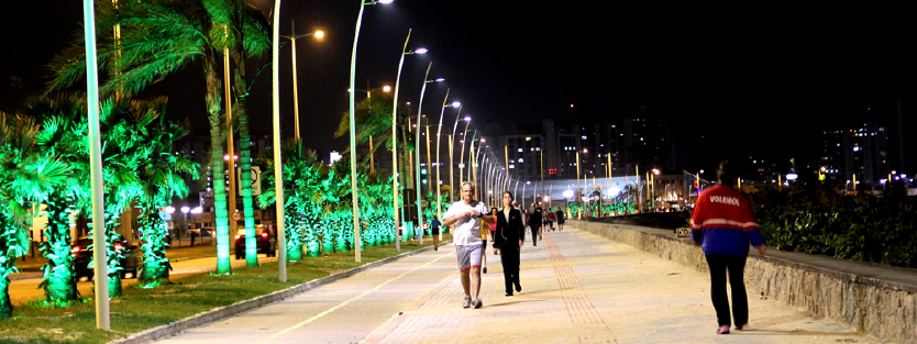 Imagem noturna da Beira Mar, onde pessoas caminham na orla