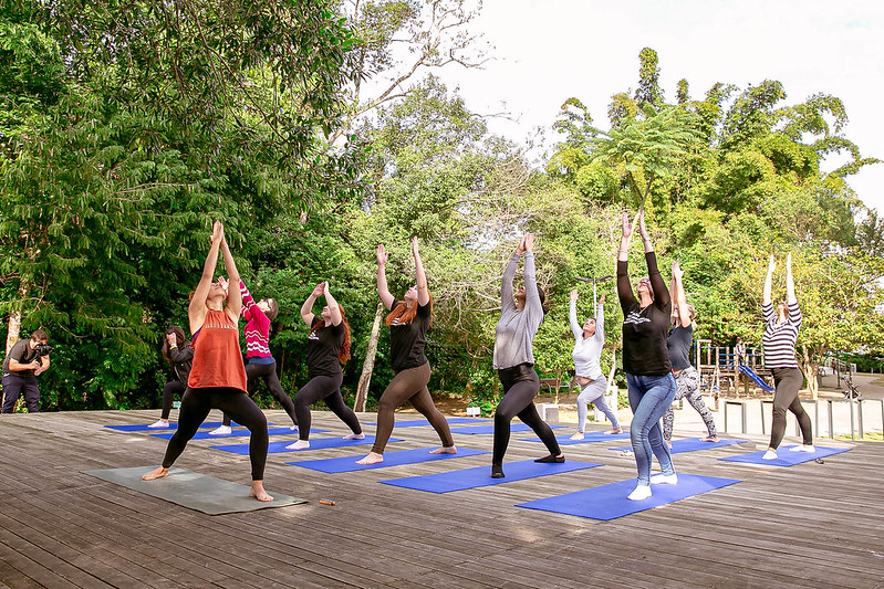 Pessoas com roupa de ginástica fazendo uma aula coletiva de yoga ao ar livre no Parque Linear do Córrego Grande