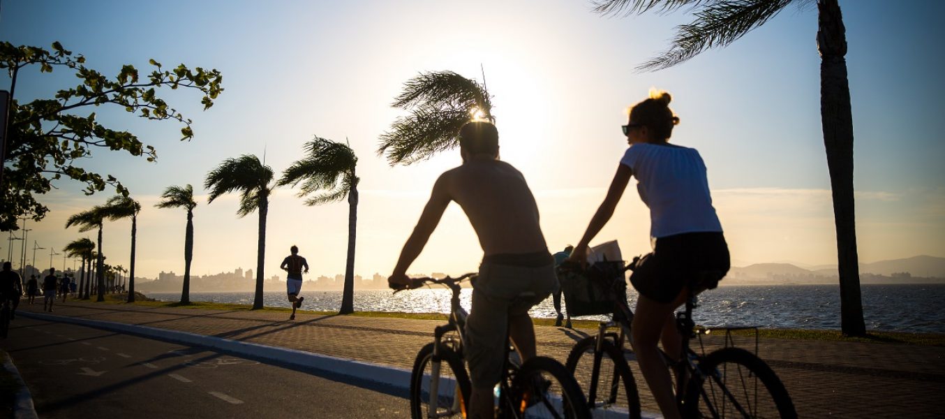 Casal pedalando na beira mar de Florianópolis, mostrando como a localização de um imóvel pode influenciar sua rotina