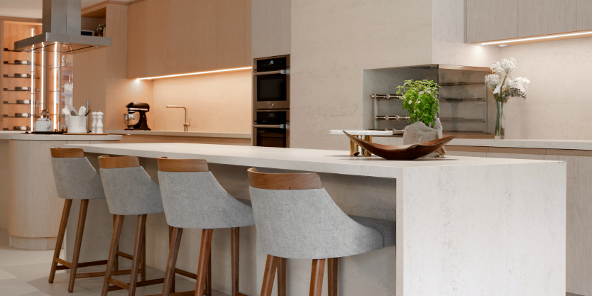 Showroom: A cozinha com ilha central, banquetas e eletrodomésticos embutidos. A iluminação e os acabamentos são planejados para criar um ambiente prático e acolhedor, refletindo um estilo de vida prático.